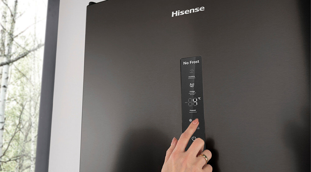 Czarna lodówka z logo \'Hisense\' i panelem dotykowym z napisem \'No Frost\'. Osoba dotyka panelu sterowania na drzwiach lodówki.