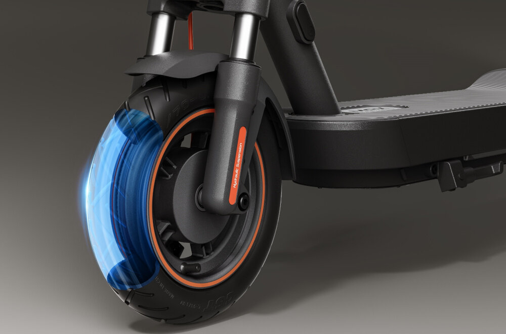 Zbliżenie na przednie koło czarnej hulajnogi elektrycznej z pomarańczowym akcentem na oponie i widocznym napisem \'XIAOMI Scooter\'.