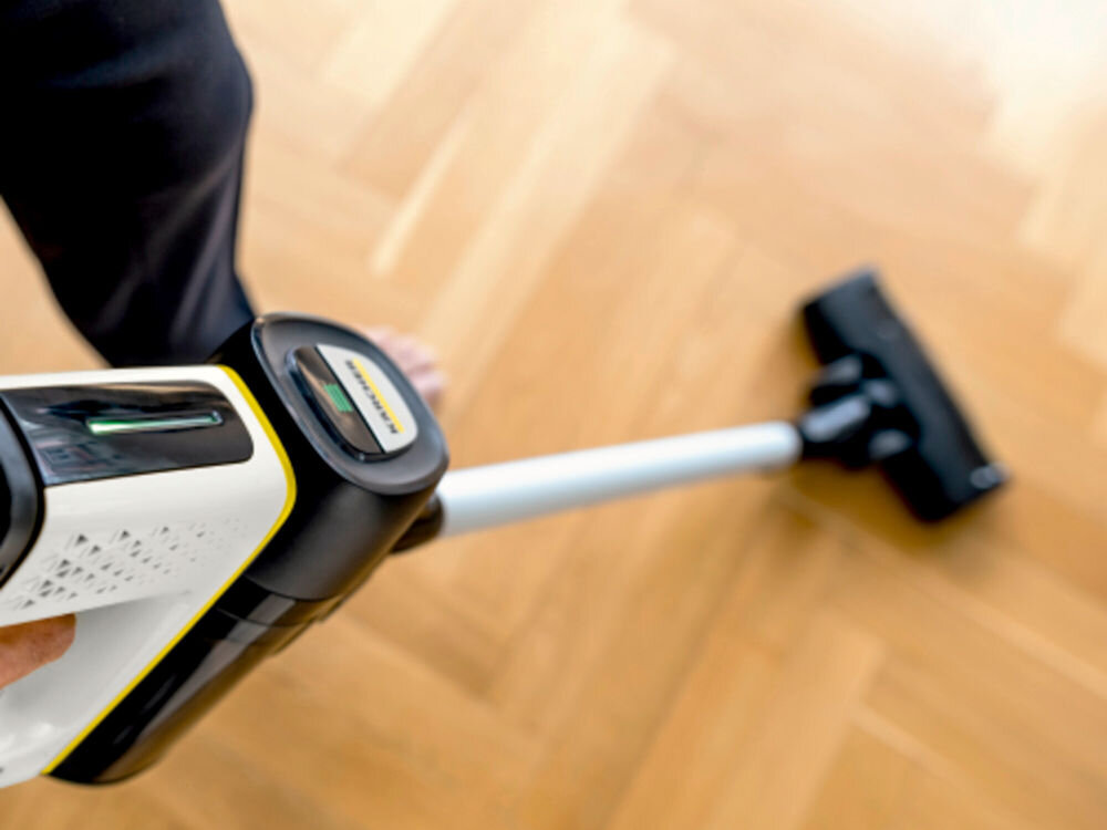 Osoba używa odkurzacza pionowego na drewnianej podłodze. Na odkurzaczu widoczne jest logo \'KARCHER\'.