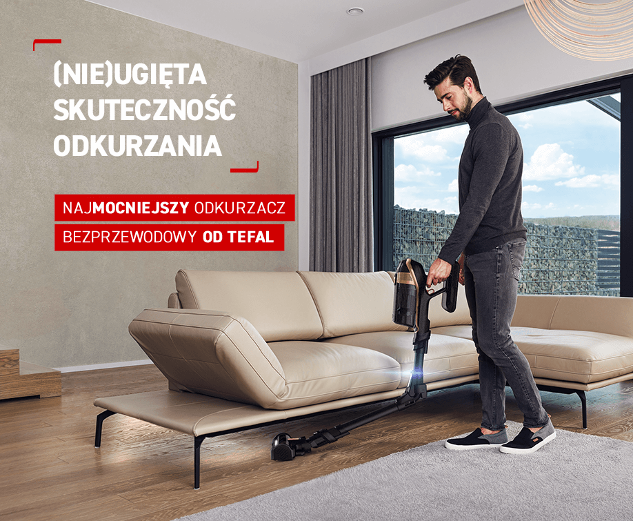 Mężczyzna używa odkurzacza w salonie z beżową sofą i dużym oknem. Tekst na obrazie: \'(NIE)UGIĘTA SKUTECZNOŚĆ ODKURZANIA NAJMOCNIEJSZY ODKURZACZ BEZPRZEWODOWY OD TEFAL\'.