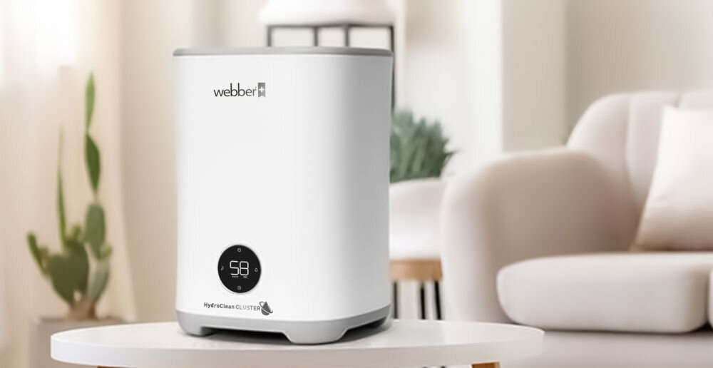 Na zdjęciu znajduje się biały nawilżacz ewaporacyjny z wyświetlaczem pokazującym liczbę 58. Na urządzeniu widoczne jest logo \'webber\' oraz napis \'HydroClean CLUSTER\'.