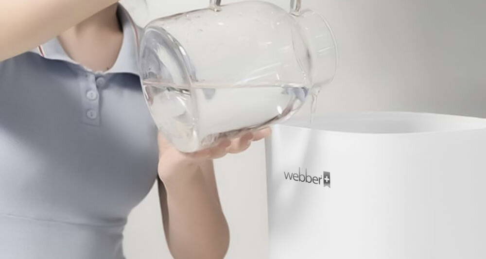 Osoba nalewa wodę z przezroczystego dzbanka do białego urządzenia z widocznym logo \'webber\'.
