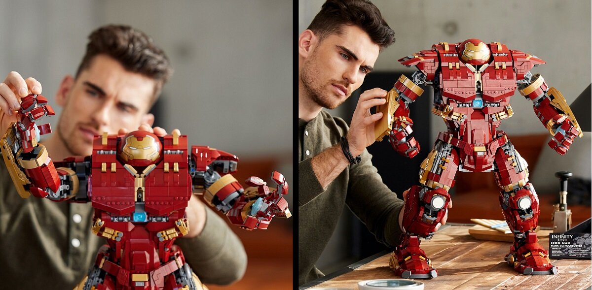 Na obrazie widać osobę składającą duży model LEGO przedstawiający czerwono-złotego robota. Model jest szczegółowy i stoi na drewnianym stole.