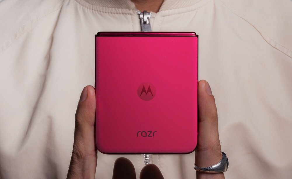 Osoba trzyma złożony, różowy telefon z widocznym logo \'M\' i napisem \'razr\'.