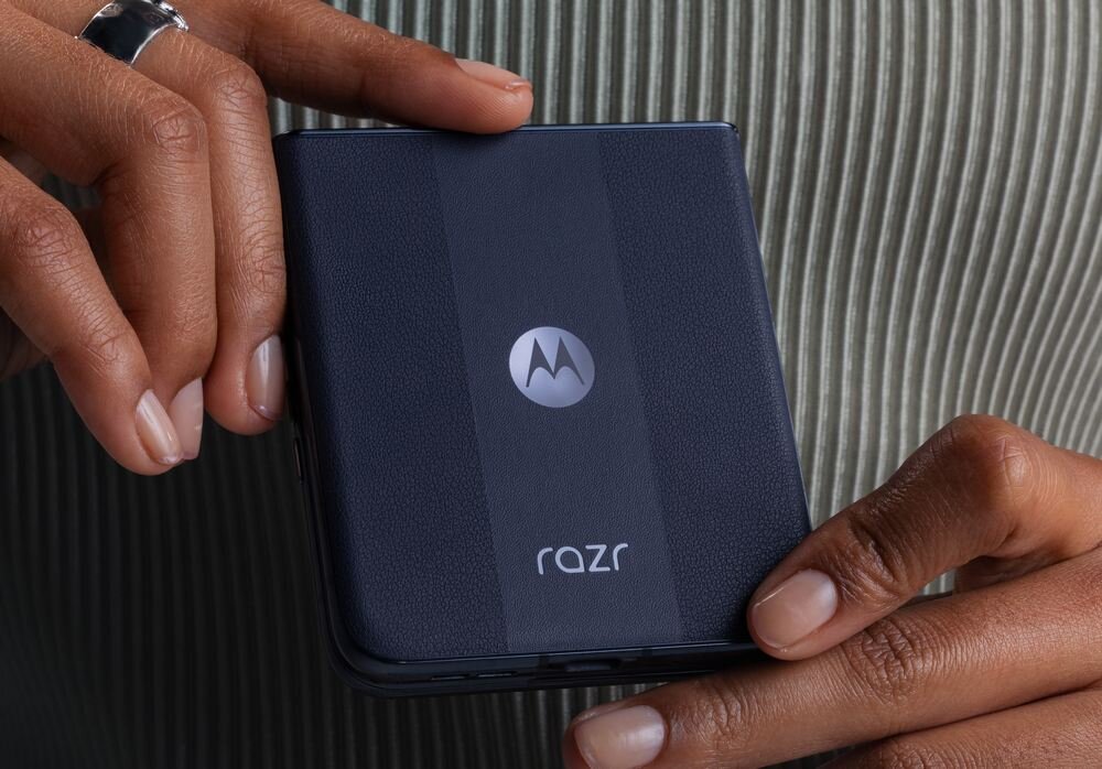Osoba trzyma złożony smartfon w kolorze granatowym z widocznym logo Motorola i napisem \'razr\'.