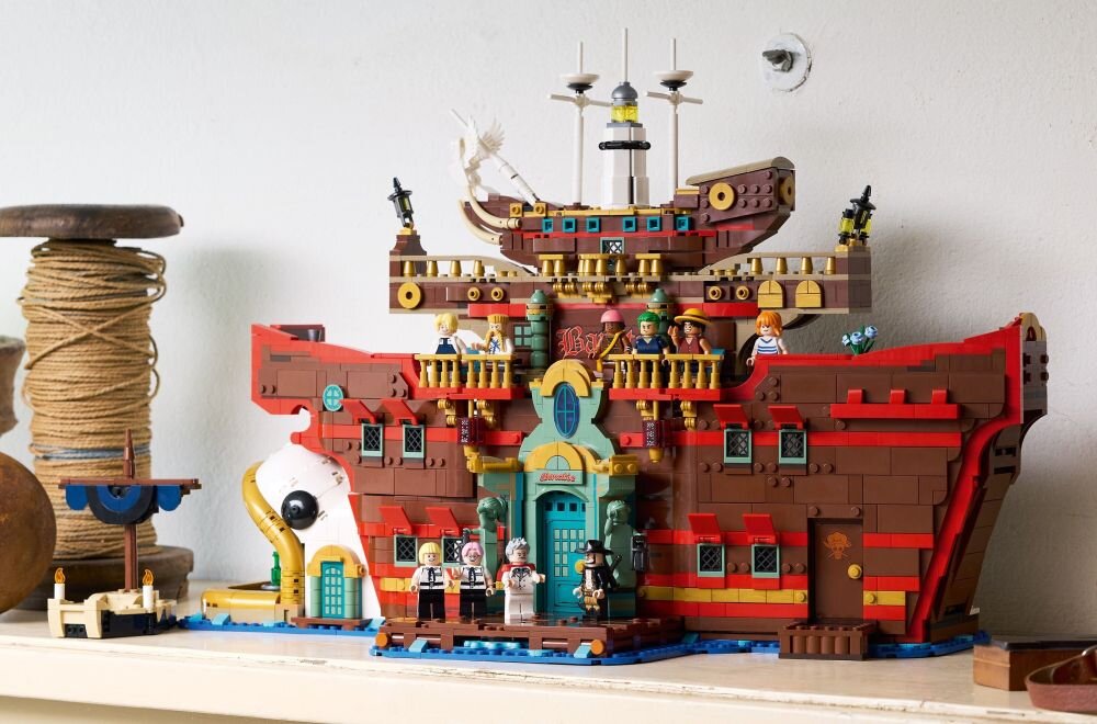 Model LEGO przedstawiający pływającą restaurację z detalami architektonicznymi i figurkami na pokładzie. W tle widoczne są elementy dekoracyjne, takie jak szpule z liną.