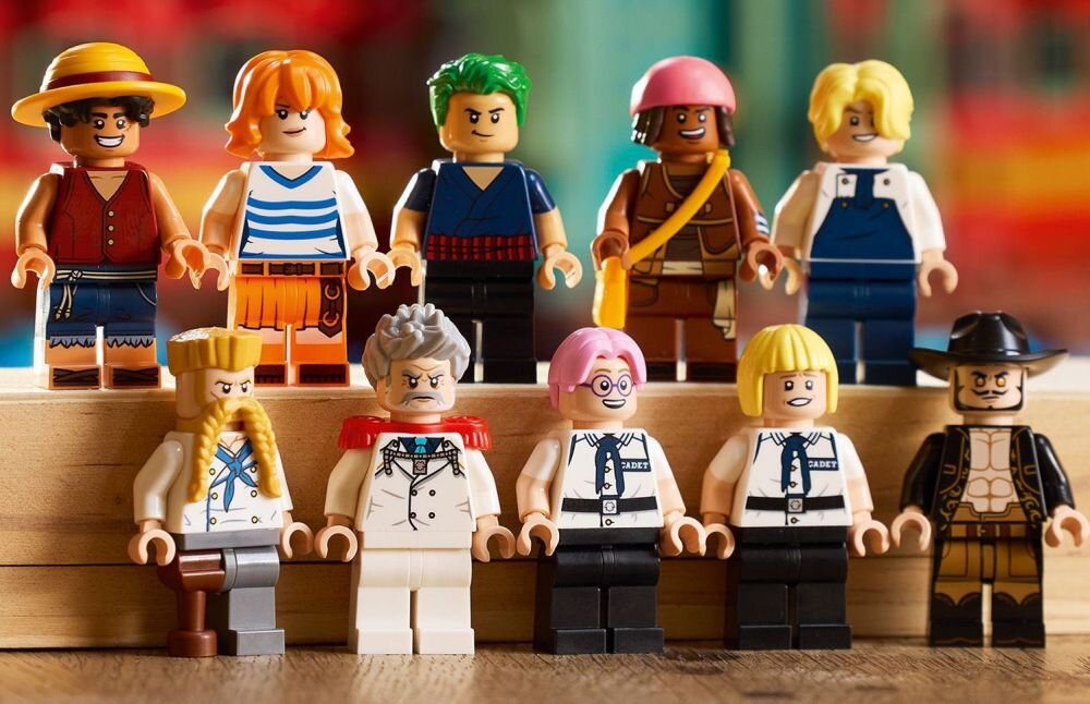 Na obrazie znajduje się dziesięć figurek LEGO przedstawiających różnorodne postacie, ustawione w dwóch rzędach na drewnianej powierzchni. Każda figurka ma unikalny strój i fryzurę, a w tle widać rozmyte kolory.