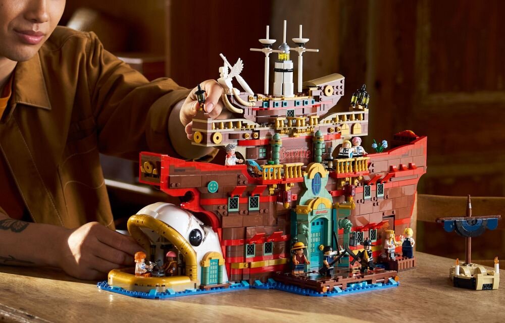 Zestaw LEGO przedstawiający pływającą restaurację z detalami architektonicznymi i figurkami. Osoba układająca zestaw siedzi przy stole.