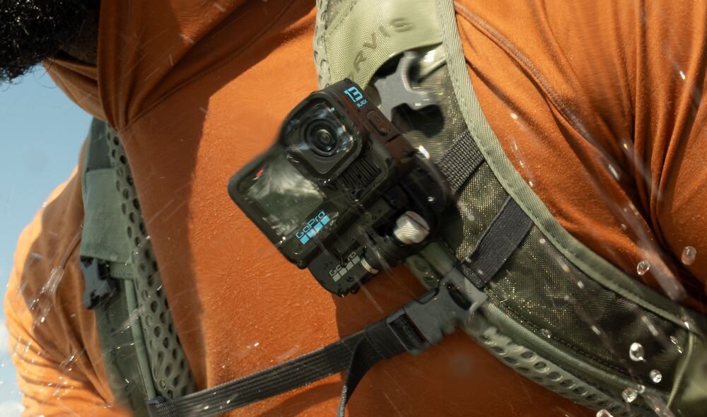 Osoba nosi kamerę sportową zamocowaną na pasku plecaka. Kamera ma widoczne logo \'GOPRO\' i jest w kolorze czarnym.