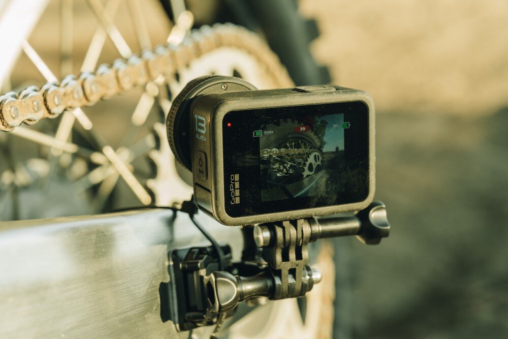 Kamera sportowa zamontowana na rowerze, z widocznym ekranem wyświetlającym obraz z rowerem. Na kamerze widoczne są napisy \'13 BLACK\' oraz \'GOPRO\'.