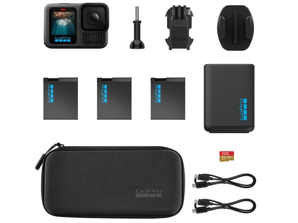 Na obrazie znajduje się zestaw akcesoriów do kamery sportowej, w tym kamera z wyświetlaczem, trzy baterie, ładowarka, uchwyty montażowe, etui z logo GoPro, karta pamięci SanDisk 64 GB oraz dwa kable USB.