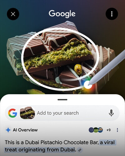 Obraz przedstawia aplikację Google z funkcją wyszukiwania wizualnego, pokazującą baton czekoladowy z pistacjami. Na ekranie widoczny jest tekst: \'This is a Dubai Pistachio Chocolate Bar, a viral treat originating from Dubai.\'