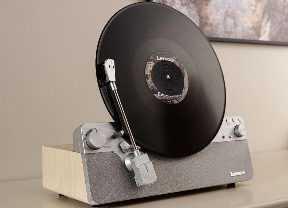 Gramofon z czarną płytą winylową na drewnianej podstawie, z widocznym logo \'Lenco\' na obudowie. Na płycie widoczny jest napis \'Enjoy music\'.
