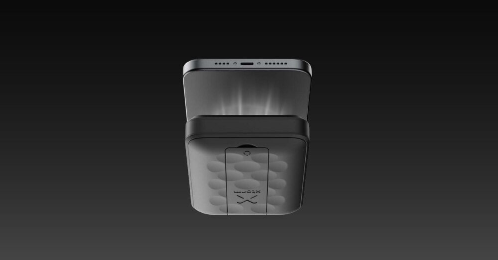 Czarny powerbank z logo \'XTORM\' i wzorem okręgów na powierzchni, umieszczony pod smartfonem na ciemnym tle.