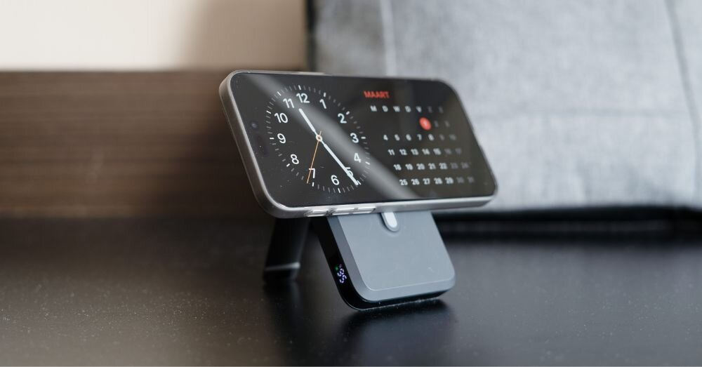 Na zdjęciu widać smartfon ustawiony na stojaku, wyświetlający zegar analogowy i kalendarz. Stojak jest czarny i ma prosty, nowoczesny design.