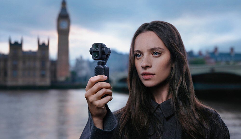 Kamera sportowa DJI Osmo Pocket 4P Młoda kobieta stojąca na tle rzeki i wieży zegarowej Big Ben w Londynie trzyma w dłoni kompaktową kamerę