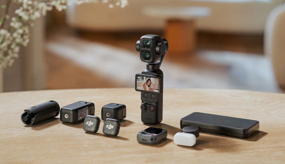 Kamera sportowa DJI Osmo Pocket 4P Kamera na gimbalu ustawiona na stole w otoczeniu zestawu akcesoriów takich jak mikrofony bezprzewodowe i etui