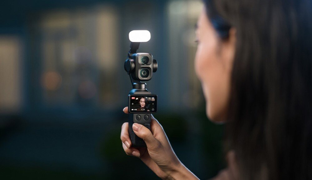 Kamera sportowa DJI Osmo Pocket 4P Kobieta trzyma w dłoni kamerę z włączoną lampą doświetlającą zamontowaną na górze urządzenia podczas nagrywania w ciemnym otoczeniu