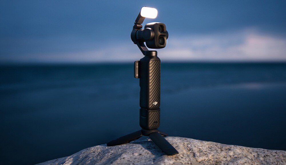 Kamera sportowa DJI Osmo Pocket 4P Mała kamera z włączonym dodatkowym oświetleniem ustawiona na małym statywie na skale nad brzegiem morza