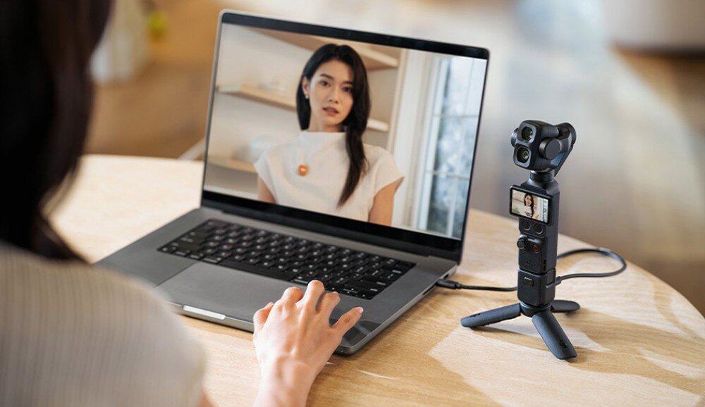Kamera sportowa DJI Osmo Pocket 4P Kamera na małym statywie podłączona do laptopa wyświetlającego obraz wideo przedstawiający kobietę