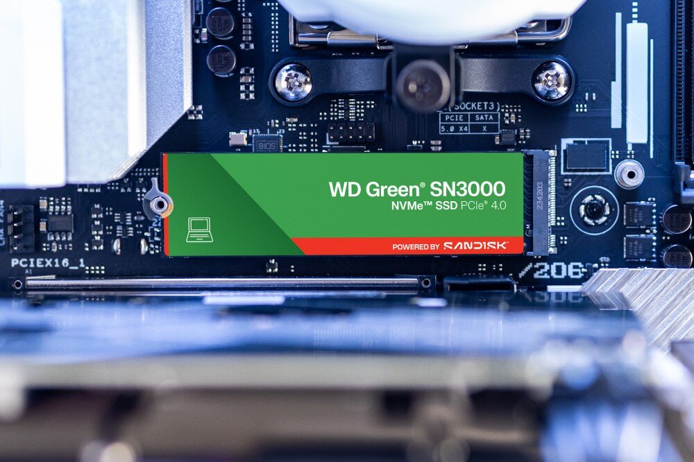 Na obrazie widoczny jest dysk SSD z napisem \'WD Green SN3000 NVMe SSD PCIe 4.0\' oraz logo \'SANDISK\', zamontowany na płycie głównej komputera.