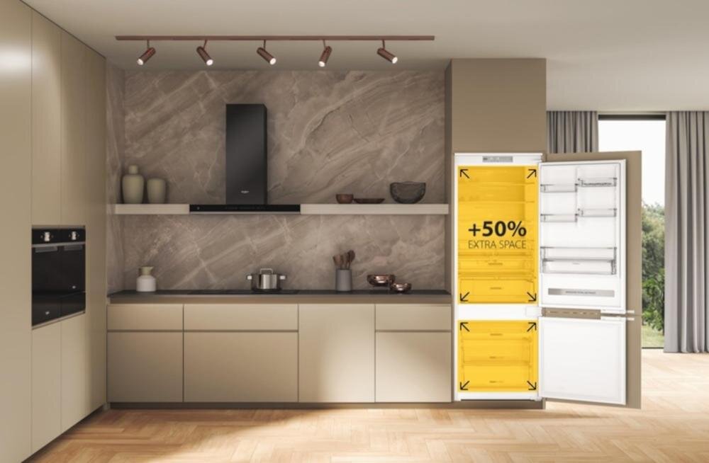 Kuchnia z nowoczesnymi szafkami i otwartą lodówką, na której drzwiach widnieje napis \'+50% EXTRA SPACE\'. Wnętrze lodówki jest jasne, a na półkach znajdują się przezroczyste pojemniki.