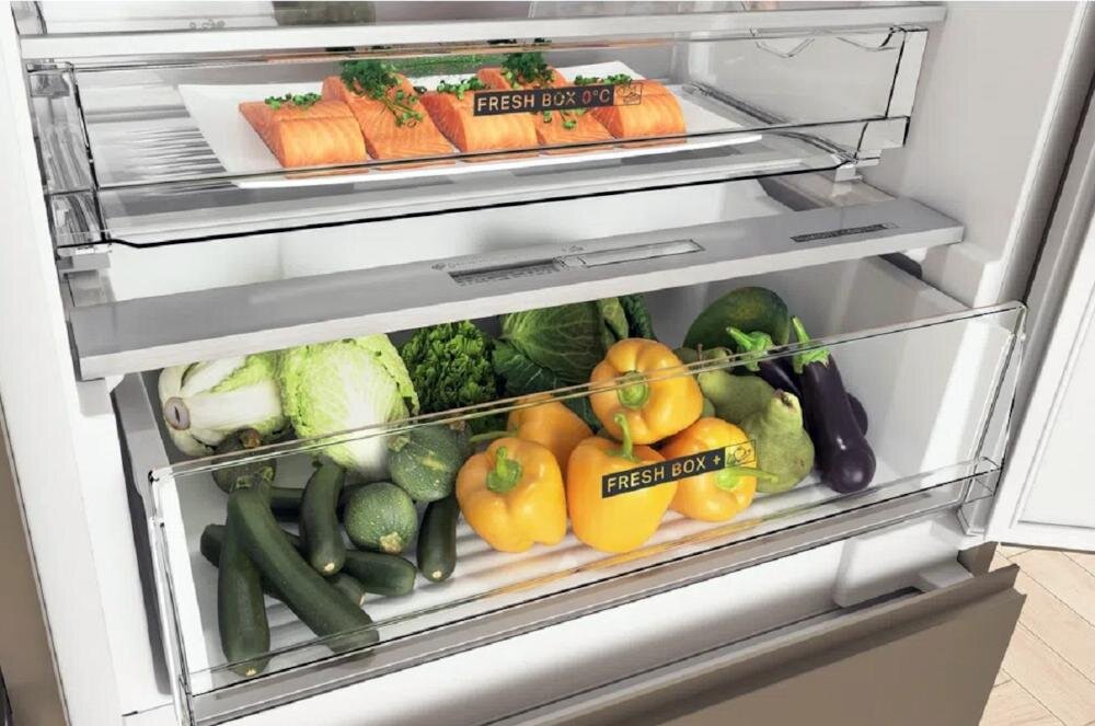 Wnętrze lodówki z dwoma szufladami oznaczonymi jako \'FRESH BOX\'. W górnej szufladzie znajdują się kawałki łososia, a w dolnej różne warzywa, w tym papryki i cukinie.