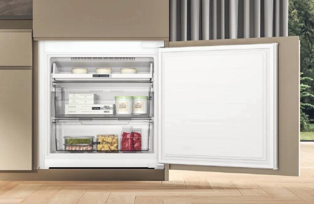 Otwarta lodówka z trzema półkami, na których znajdują się różne produkty spożywcze, w tym pojemniki z lodami i warzywami. Drzwi lodówki są białe, a wnętrze jest dobrze oświetlone.