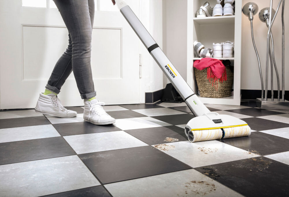 Osoba używa elektrycznego mopa na czarno-białej podłodze w pomieszczeniu. Na mopie widoczne jest logo \'Karcher\'.