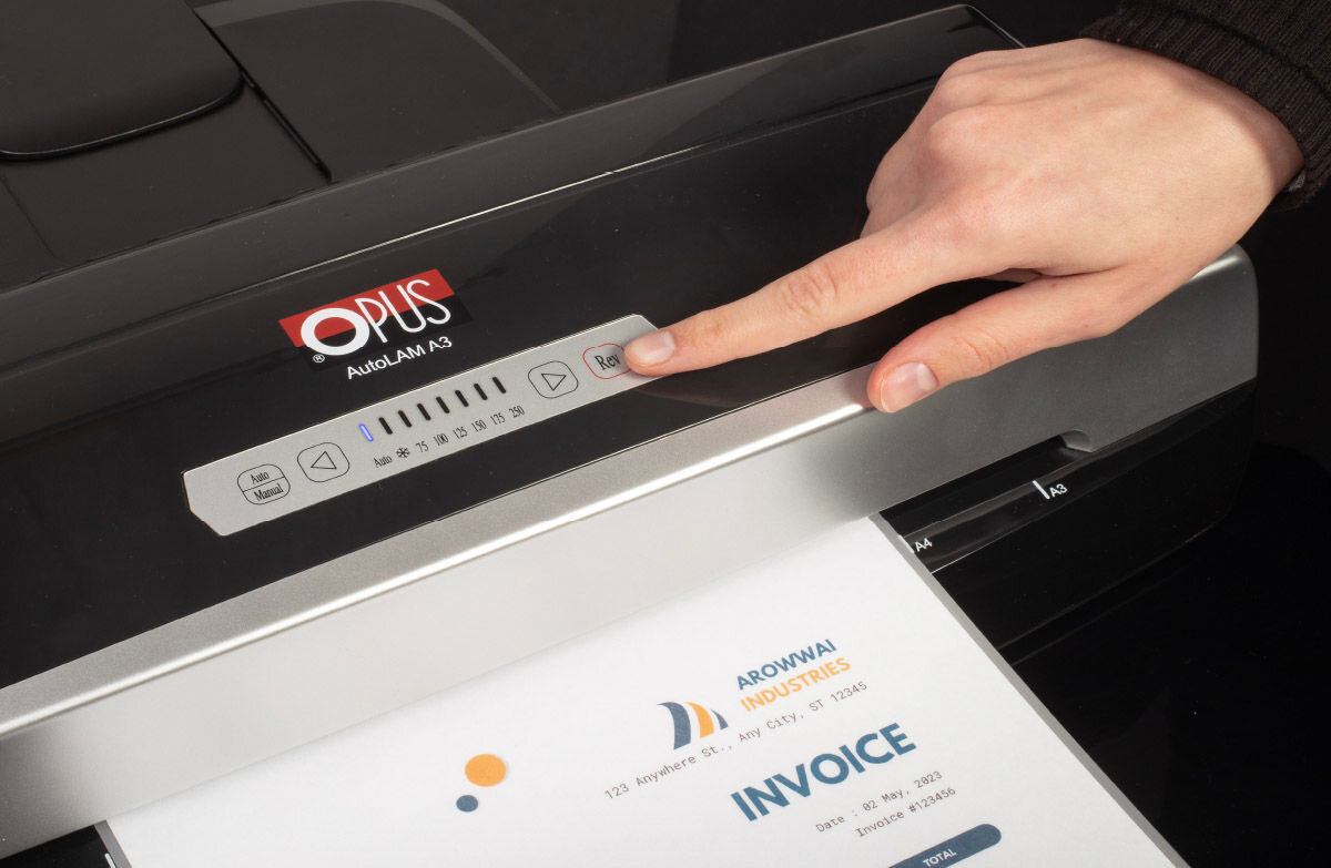 Laminator z logo \'OPUS\' i napisem \'AutoLAM A3\' na panelu sterowania, z którego wystaje zalaminowany dokument z napisem \'INVOICE\'. Osoba dotyka przycisku na panelu urządzenia.