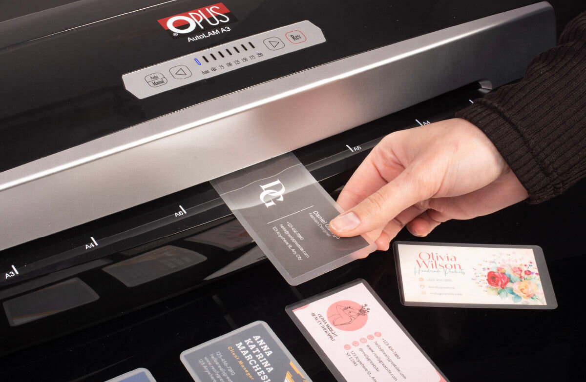 Osoba wkłada wizytówkę do laminatora OPUS autoLAM A3. Na laminatorze widoczne są przyciski sterujące i logo OPUS.
