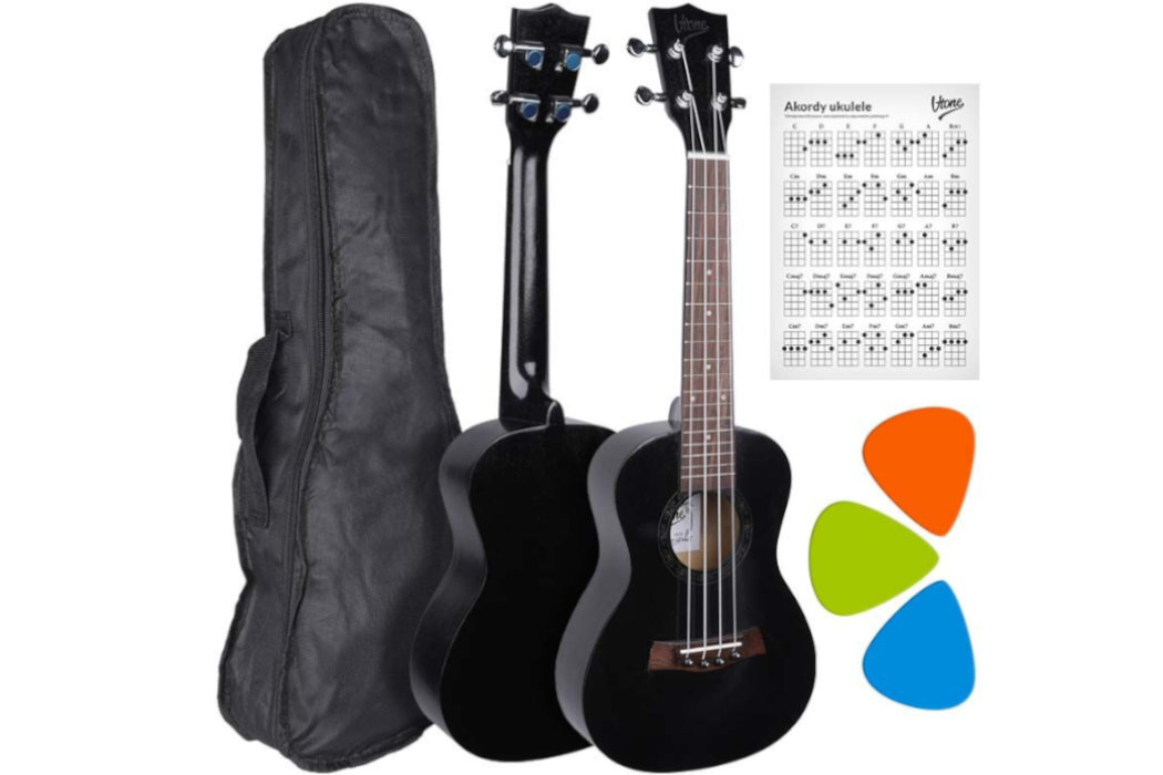 Na obrazie znajduje się czarne ukulele koncertowe z widocznym logo \'V-TONE\', pokrowiec, karta z akordami ukulele oraz trzy kolorowe kostki do gry: pomarańczowa, zielona i niebieska.