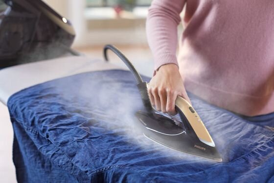 Osoba prasuje niebieską tkaninę za pomocą żelazka parowego z widocznym logo PHILIPS. Z żelazka wydobywa się para.
