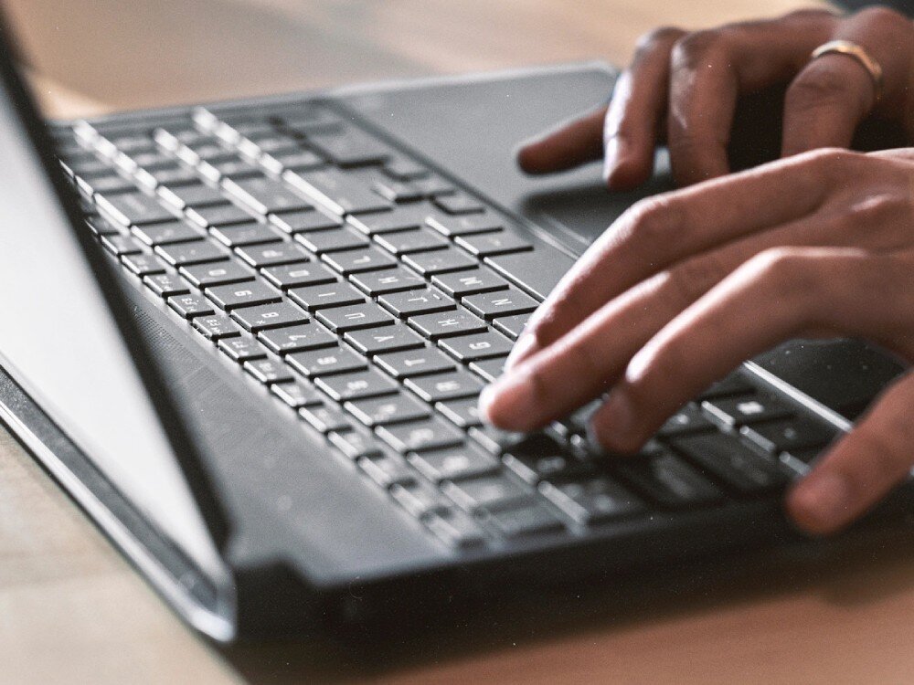 Osoba pisze na klawiaturze laptopa, widoczne są dłonie i część klawiatury.