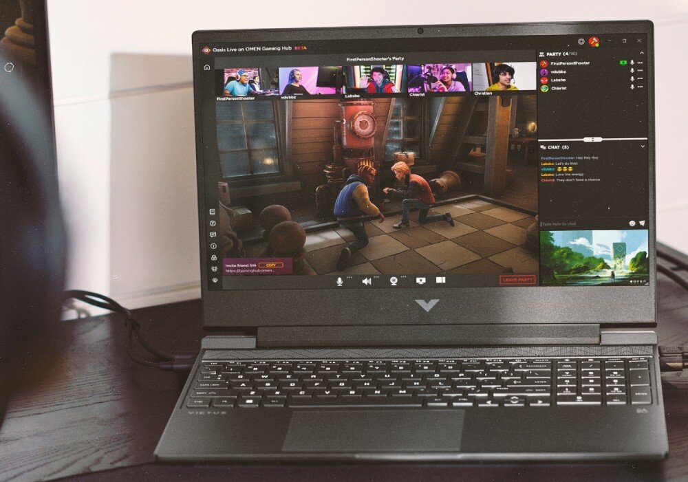 Na zdjęciu widać otwarty laptop z wyświetlonym na ekranie interfejsem gry oraz czatem wideo. Na obudowie laptopa widoczne jest logo w kształcie litery V.