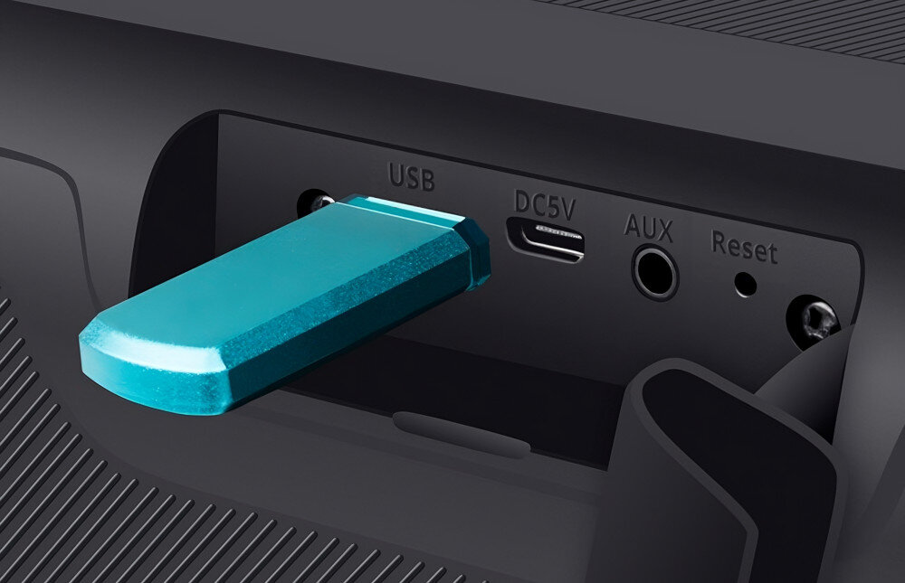 Zbliżenie na panel złącz urządzenia z widocznym niebieskim pendrive\'em w porcie USB. Obok znajdują się złącza oznaczone jako DC5V, AUX, Reset oraz okrągły przycisk.
