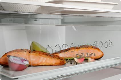 Wnętrze lodówki z półką, na której znajdują się kawałki łososia, kawałek cebuli i plasterek cytryny. Na szklanej ściance widoczny jest napis \'Chill Zone\' oraz rysunki owoców i warzyw.