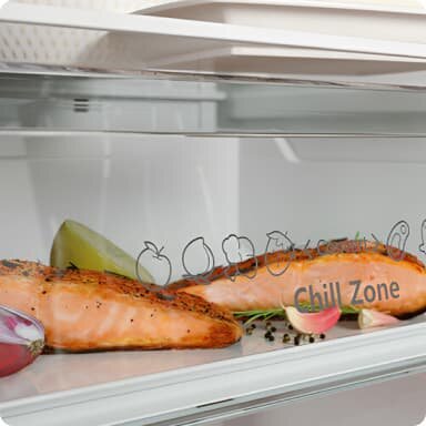 Wnętrze lodówki z przezroczystą szufladą oznaczoną napisem \'Chill Zone\', w której znajdują się kawałki łososia i plasterek cytryny. Na szufladzie widoczne są ikony owoców i warzyw.