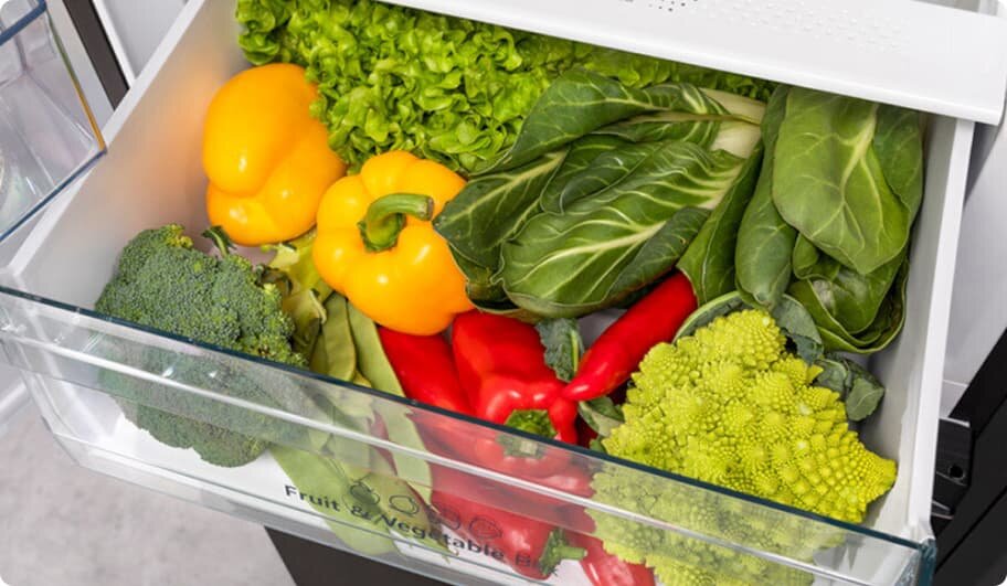 Szuflada lodówki wypełniona świeżymi warzywami, takimi jak papryka, brokuły, sałata i kapusta. Na szufladzie widoczny jest napis \'Fruit & Vegetable Box\'.