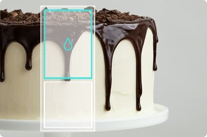Tort pokryty białym kremem z ciemną czekoladą spływającą po bokach i posypką z kawałków czekolady na wierzchu. Na obrazie widoczny jest również niebieski symbol kropli wody w prostokątnym obramowaniu.