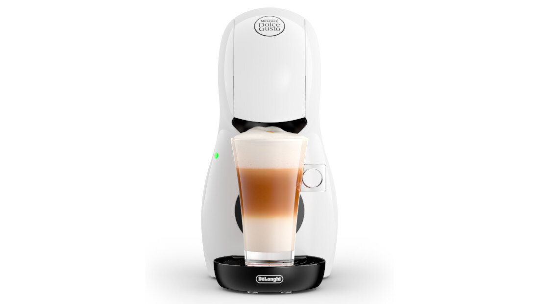 Biały ekspres do kawy z logo \'Dolce Gusto\' na górze i \'DeLonghi\' na podstawie, z przezroczystą szklanką wypełnioną kawą z mlekiem na tacy.