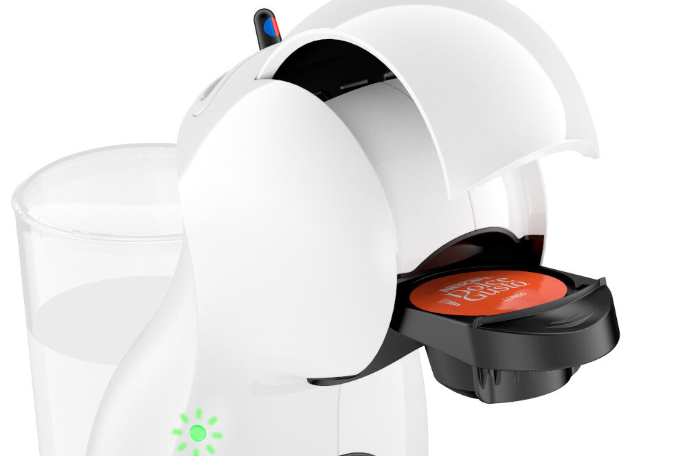 Biały ekspres do kawy z otwartą komorą na kapsułki, w której znajduje się kapsułka z napisem \'Dolce Gusto\'. W tle widoczny jest przezroczysty pojemnik na wodę.