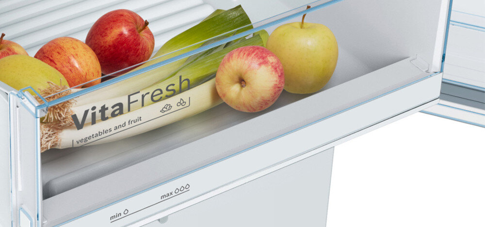 Wnętrze lodówki z szufladą oznaczoną napisem \'VitaFresh vegetables and fruit\', w której znajdują się jabłka, por i cytryna. Na szufladzie widoczne są oznaczenia \'min\' i \'max\'.