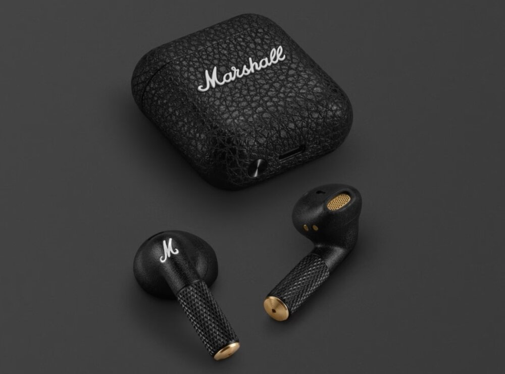 Na ciemnym tle widoczne są czarne słuchawki douszne oraz etui z teksturą, na którym znajduje się napis \'Marshall\'. Słuchawki mają złote akcenty i logo \'M\' na jednej z nich.