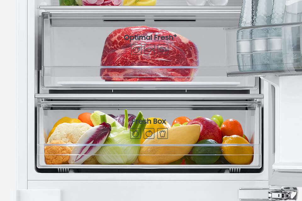 Wnętrze lodówki z dwiema szufladami; górna z napisem \'Optimal Fresh\' zawiera kawałek mięsa, dolna z napisem \'Fresh Box\' jest wypełniona różnymi warzywami i owocami.
