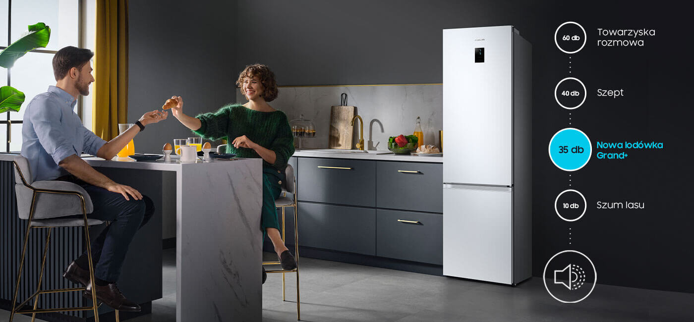 W kuchni przy stole siedzi para, a obok stoi biała lodówka. Na obrazie widoczna jest grafika z poziomami hałasu: \'60 dB Towarzyska rozmowa\', \'40 dB Szept\', \'35 dB Nowa lodówka Grand+\', \'10 dB Szum lasu\'.