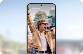 Smartfon z wyświetlaczem pokazującym osobę śpiewającą do mikrofonu, ubraną w jasną kurtkę i okulary przeciwsłoneczne. Na ekranie widoczny jest tekst \'rockwithjacket6\' oraz \'ROCK OUT\'.