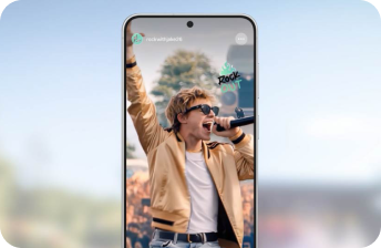 Smartfon z wyświetlaczem pokazującym osobę śpiewającą do mikrofonu, ubraną w jasną kurtkę i okulary przeciwsłoneczne. Na ekranie widoczny jest tekst \'rockwithjacket6\' oraz \'ROCK OUT\'.