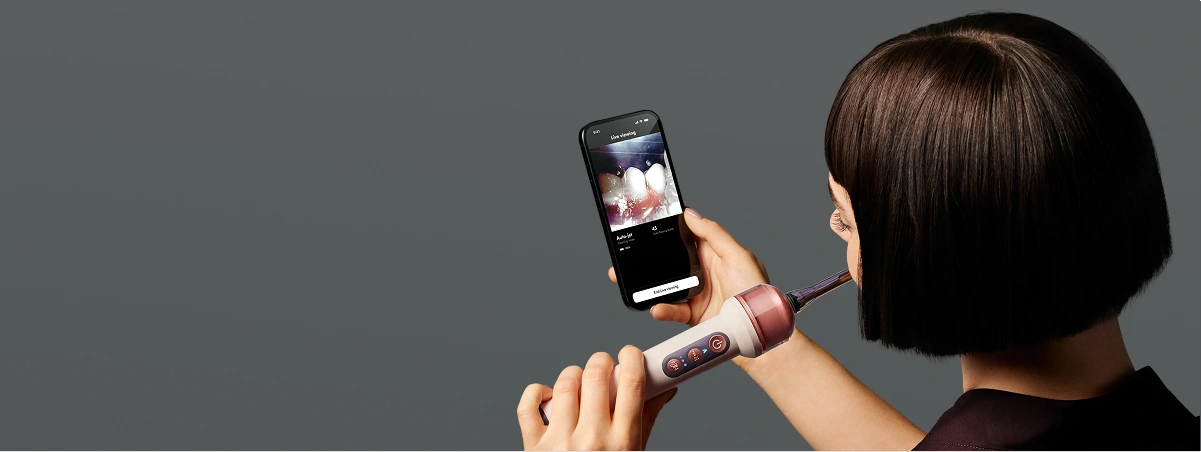 Модель чистить зуби зубною щіткою Dyson із вбудованою камерою, одночасно спостерігаючи за своїм ставленням до чищення у застосунку.