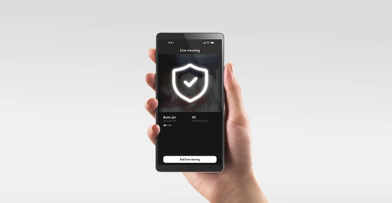Widok smartfona w dłoni z otwartą aplikacją MyDyson i ikoną bezpieczeństwa